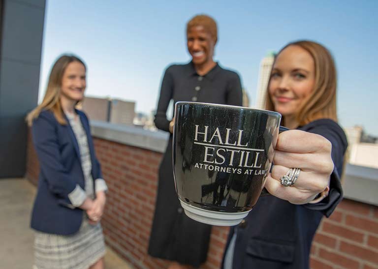 Attorneys Smiling While Holding Hall Estill Attorneys at Law Coffee Mug